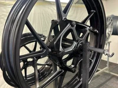 Schwarz glänzende Motorradfelgen auf Lackierständern in der Spritzkabine.